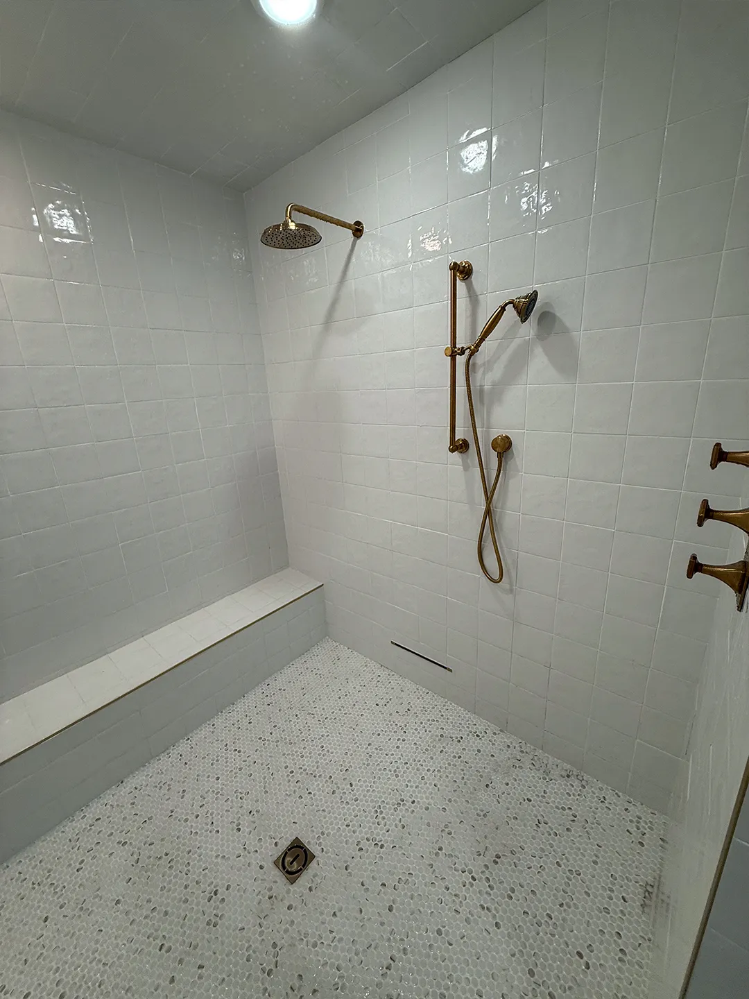 Completed walk-in shower with white tile and brass fixtures